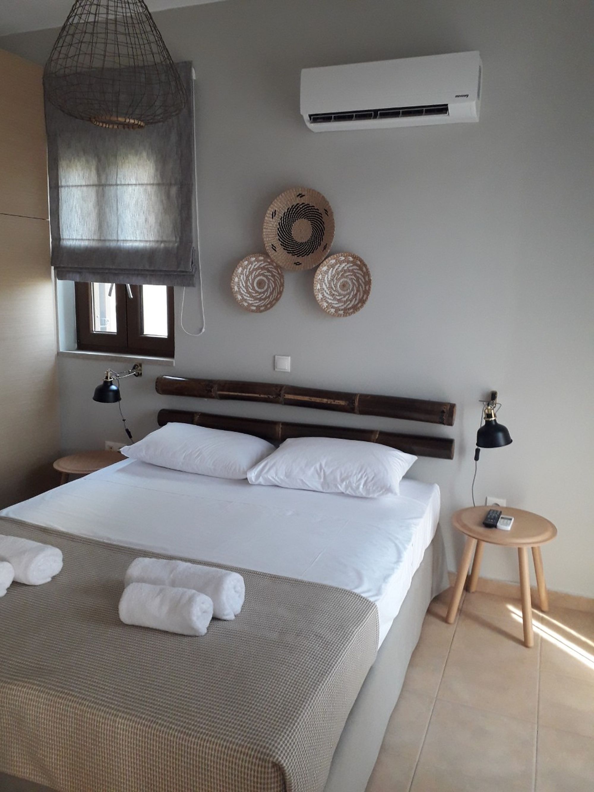Κλιματιζόμενο υπνοδωμάτιο με διπλό κρεβάτι διακοσμημένο με ιστούς μπαμπού πάνω από το κρεβάτι και τρία στρογγυλά ψάθινα διακοσμητικά στον τοίχο.