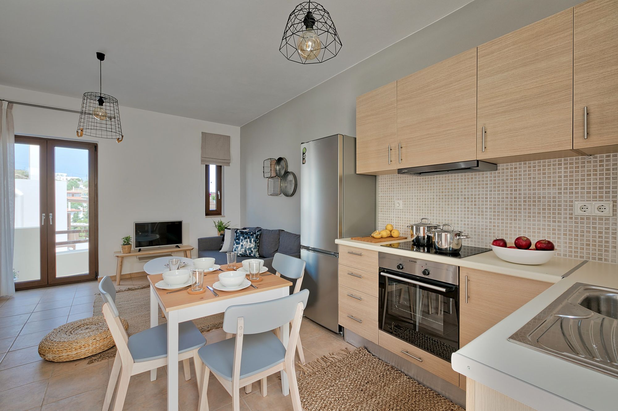 In open space with the living room, a fully equipped kitchen with an inox fridge, an electric cooker oven and a dining table with modern white dinnerware on it.