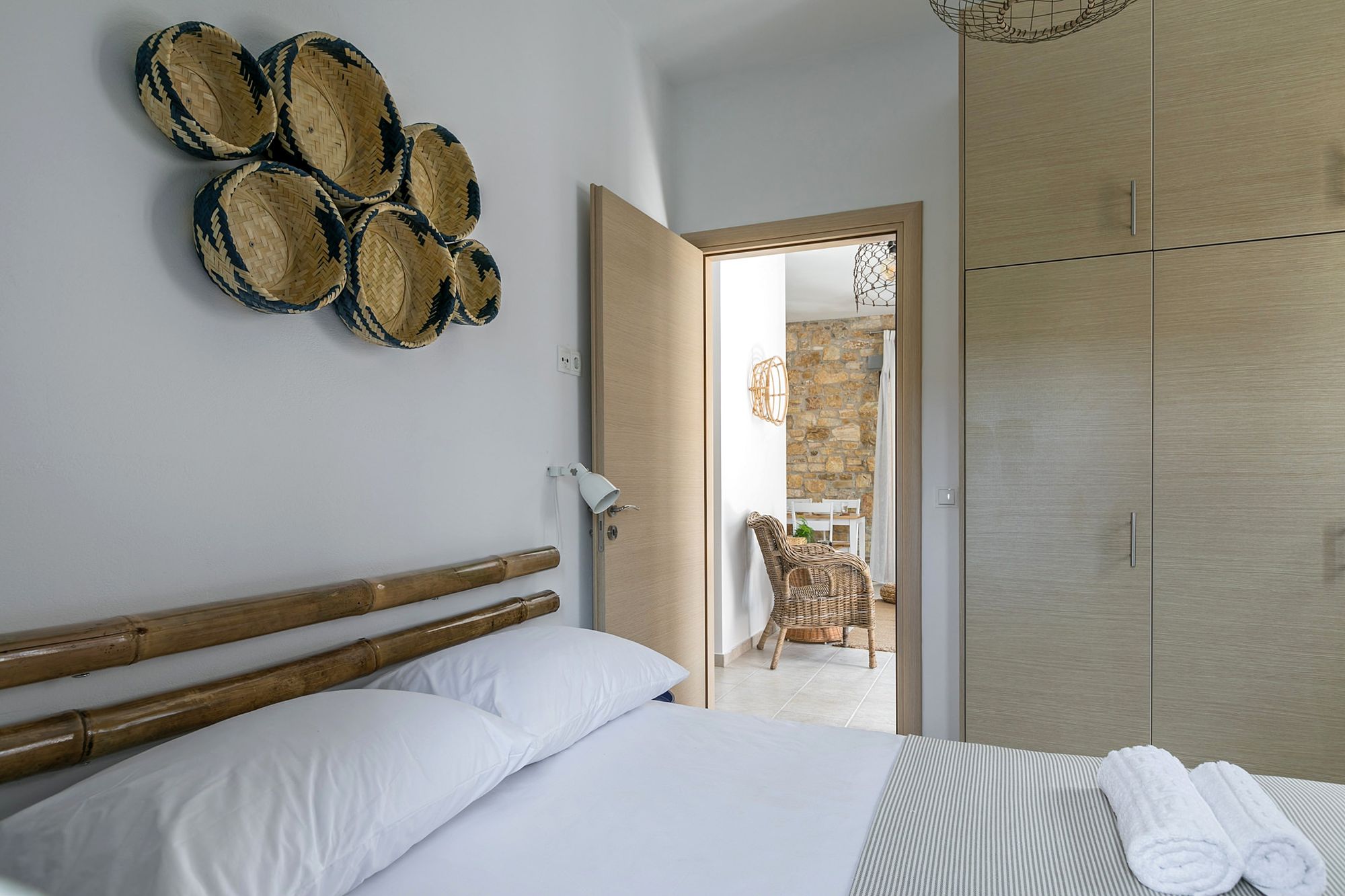 Bedroom with a double bed and decoration with bamboo masts and wicker objects on the wall over the bed.