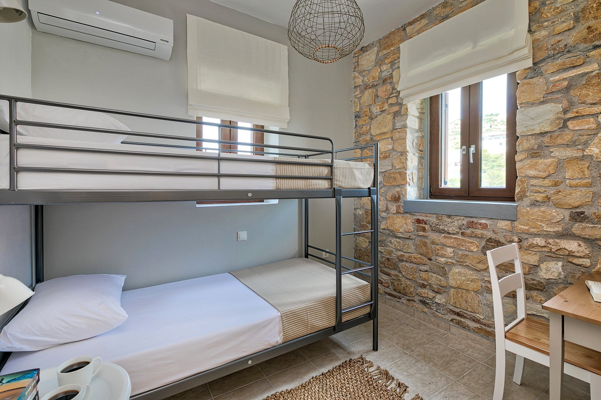 Twin stone-built bedroom with bunk beds, a bedside table and a small desk.