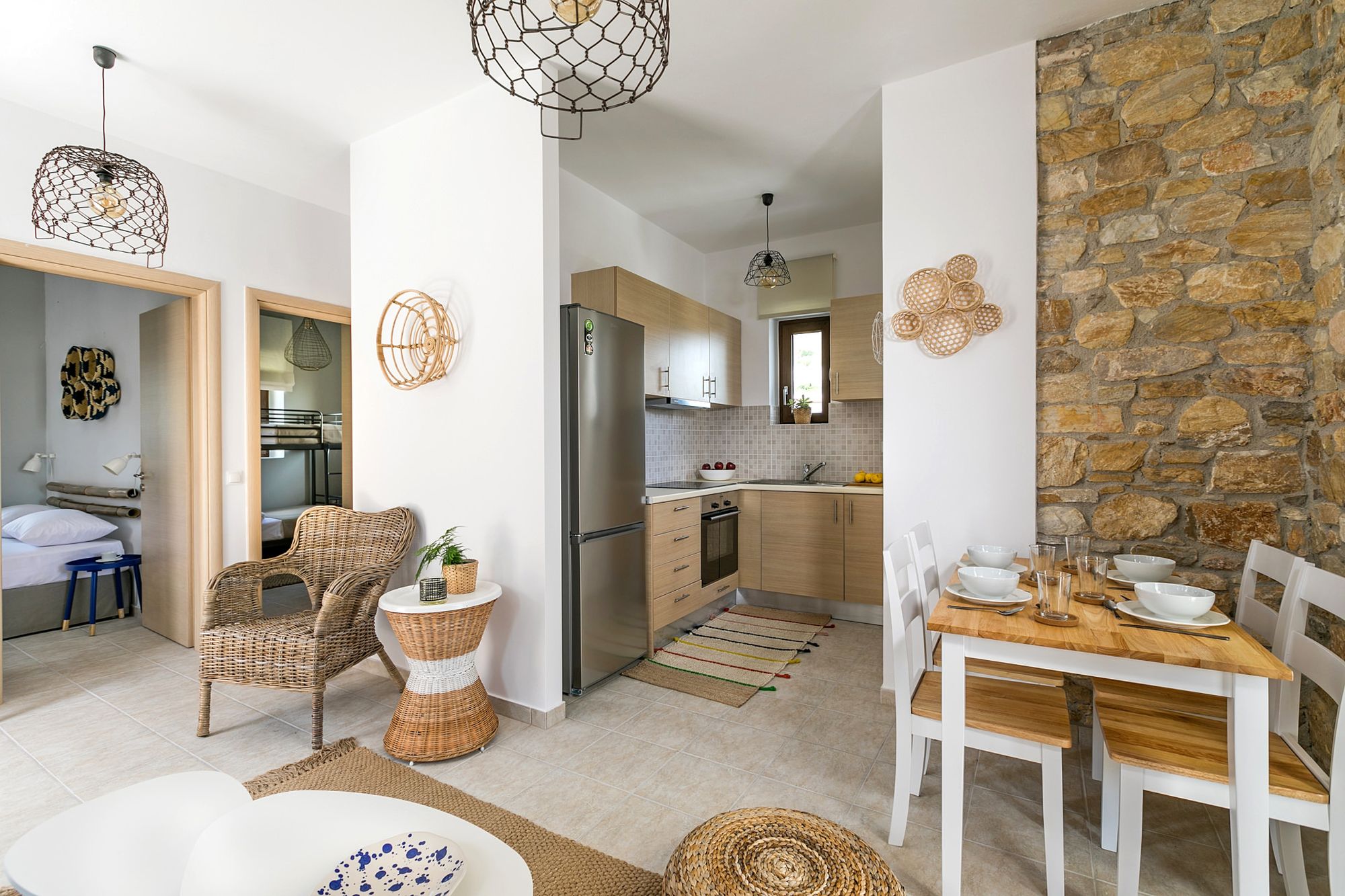 A stone-built residence decorated in boho style with two bedrooms, one with a double bed and a second one with bunk beds, a kitchen and a dining table with four chairs.