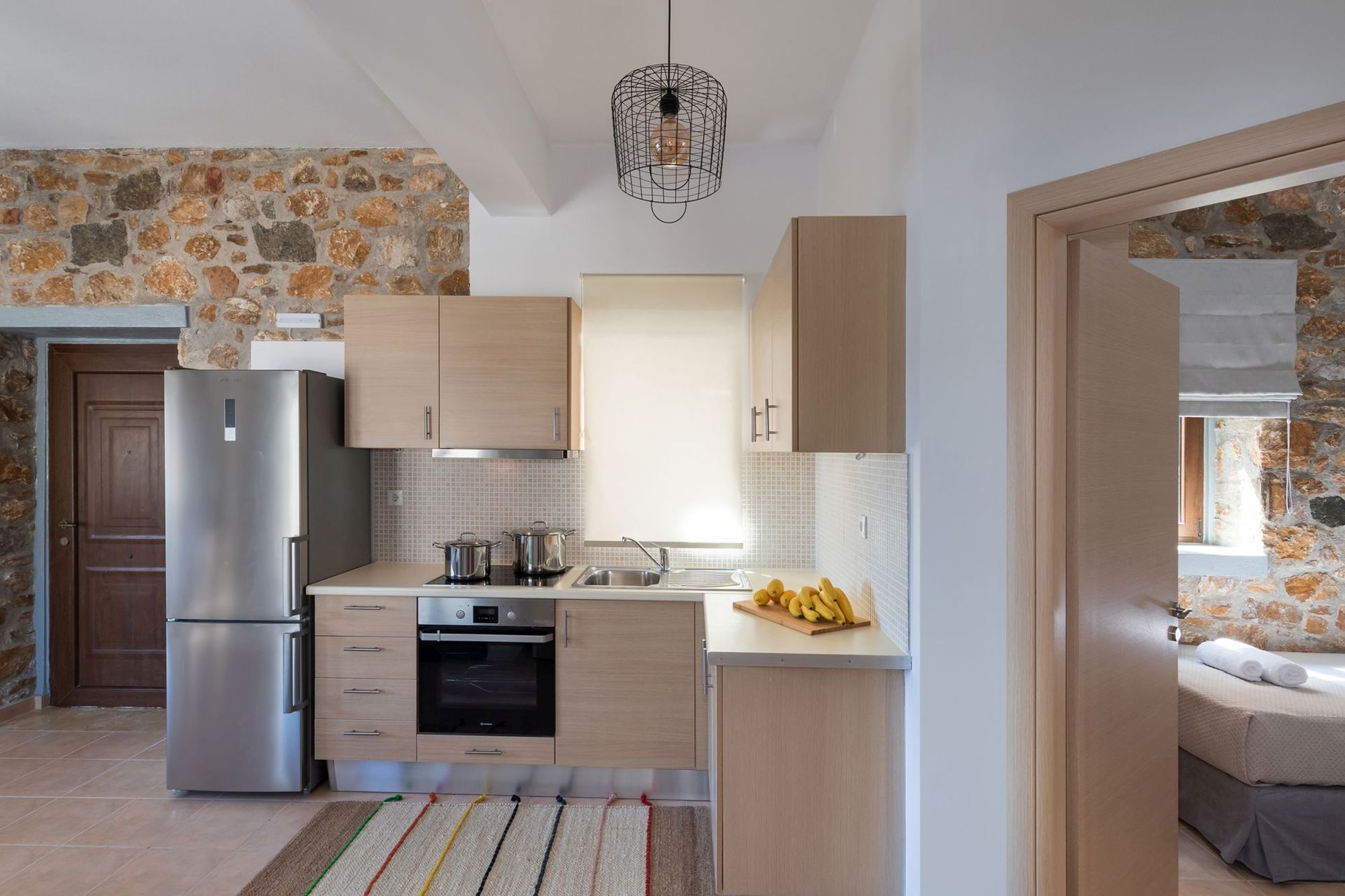 Modern kitchen in a stone built Syra Suite residence equipped with a big inox fridge and an electric cooker oven.