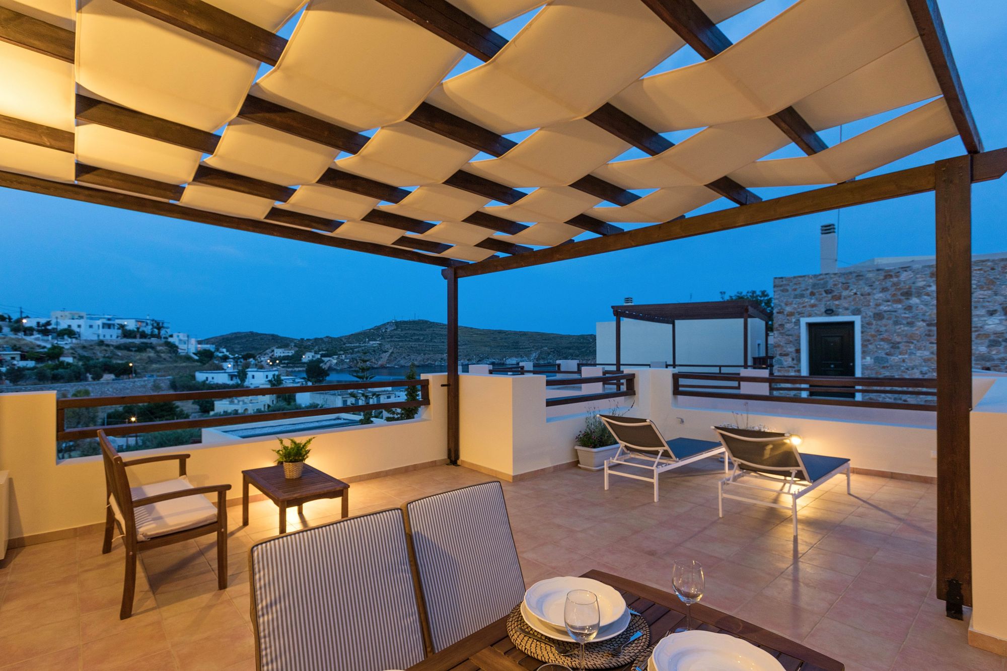 Night view of a spacious veranda furnished with lounge, two sunbeds and dining table.