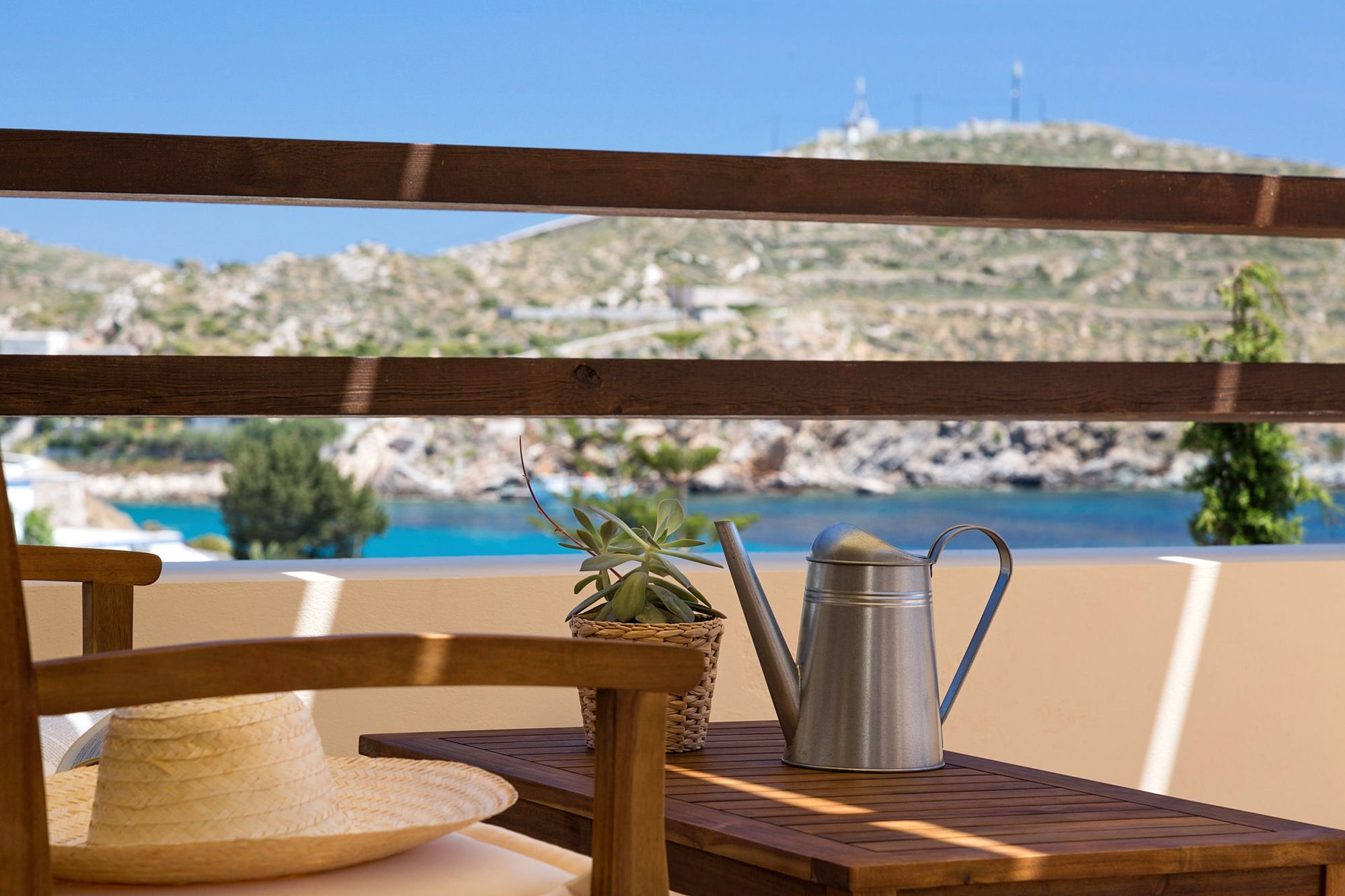 The sea view from a Syra Suite veranda furnished with an exterior sofa and a coffee table with a small decorative watering can on it.