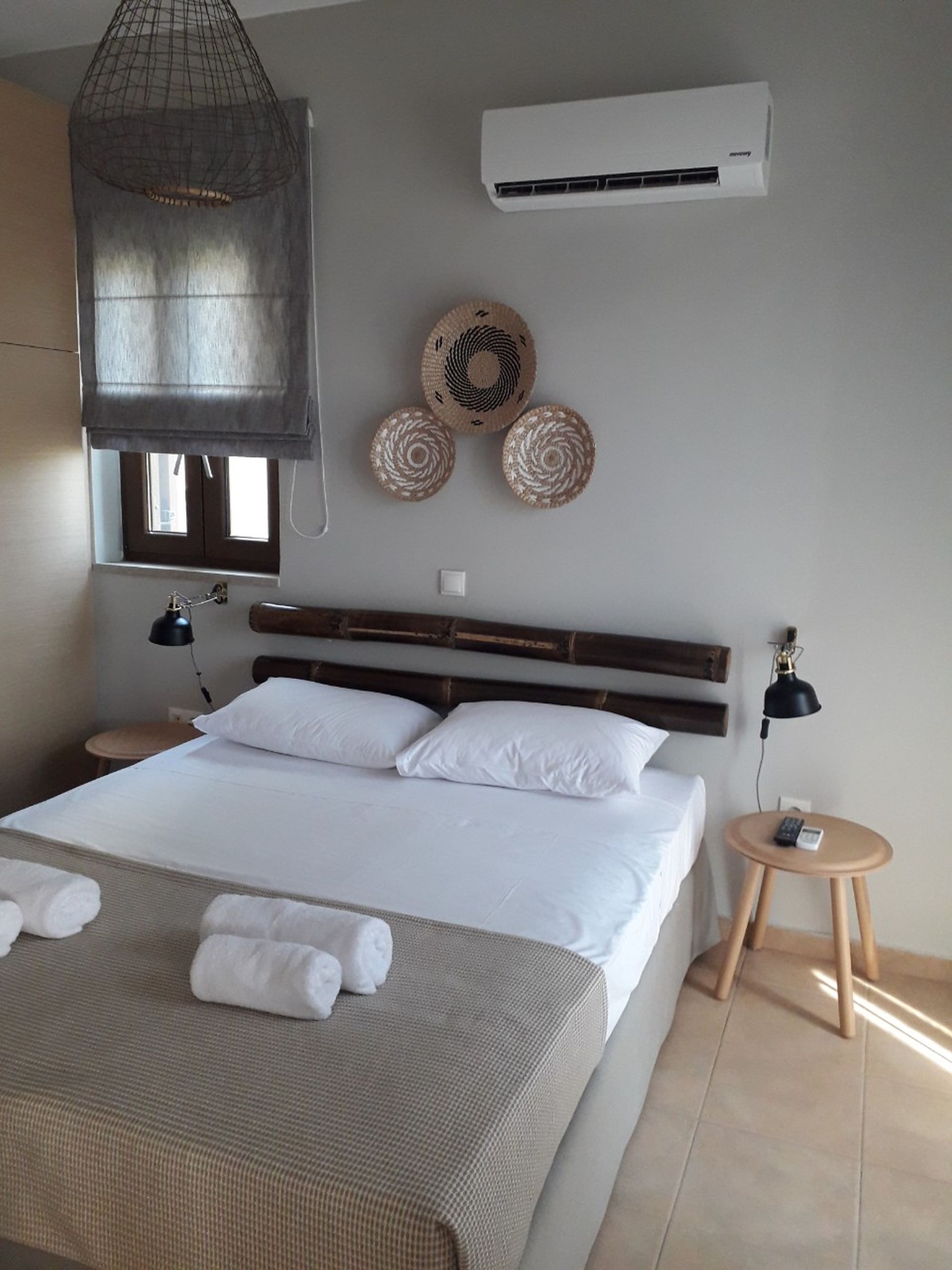 An air-conditioned bedroom with a double bed decorated with bamboo masts over the bed and three wicker round deco elements on the wall.