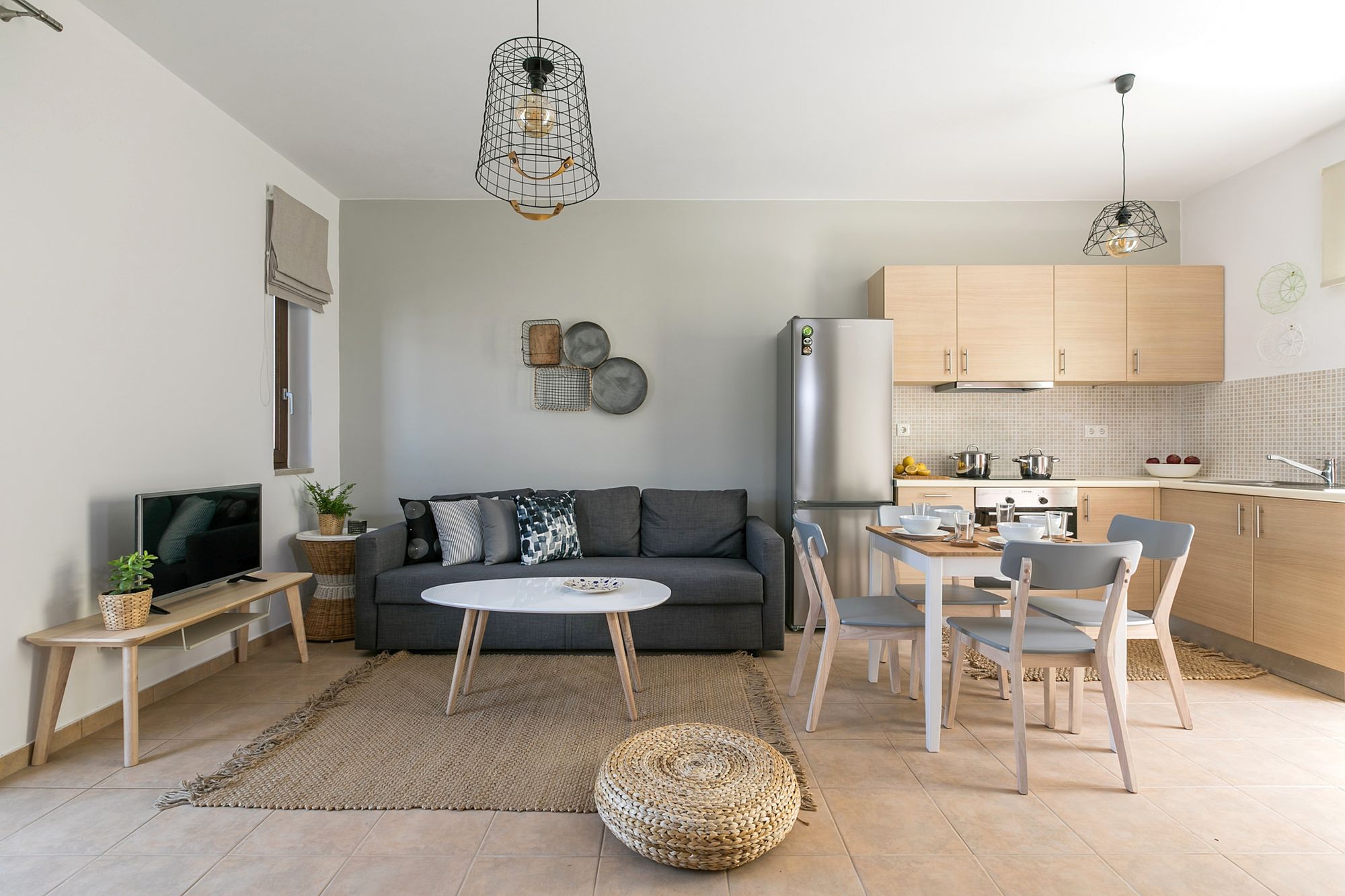 Living room with a gray sofa, a white coffee table, a flat screen TV and a wooden dining table in open space with the kitchen.