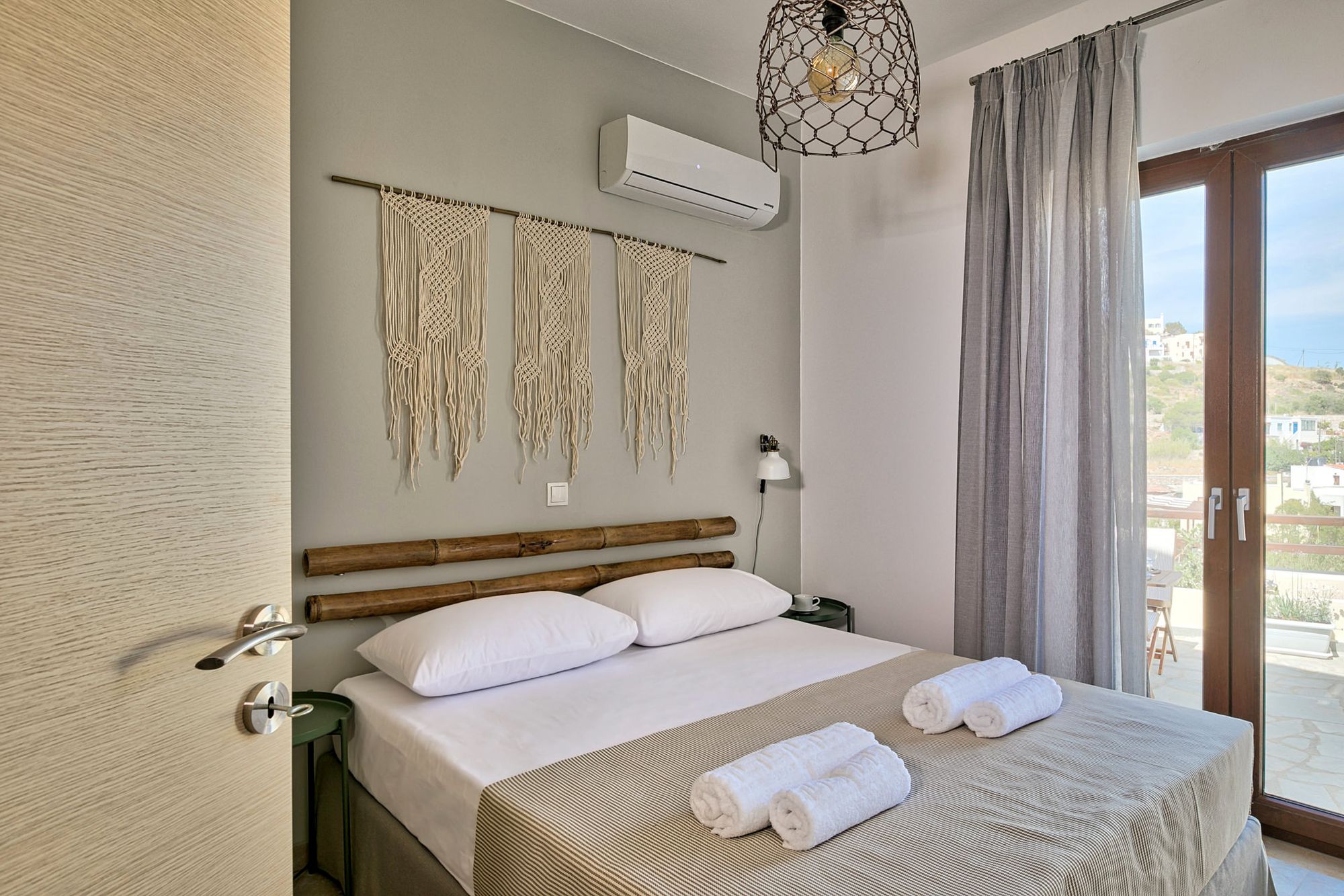 An air-conditioned bedroom with a double bed, wooden masts over the bed and a white macramé on the wall.