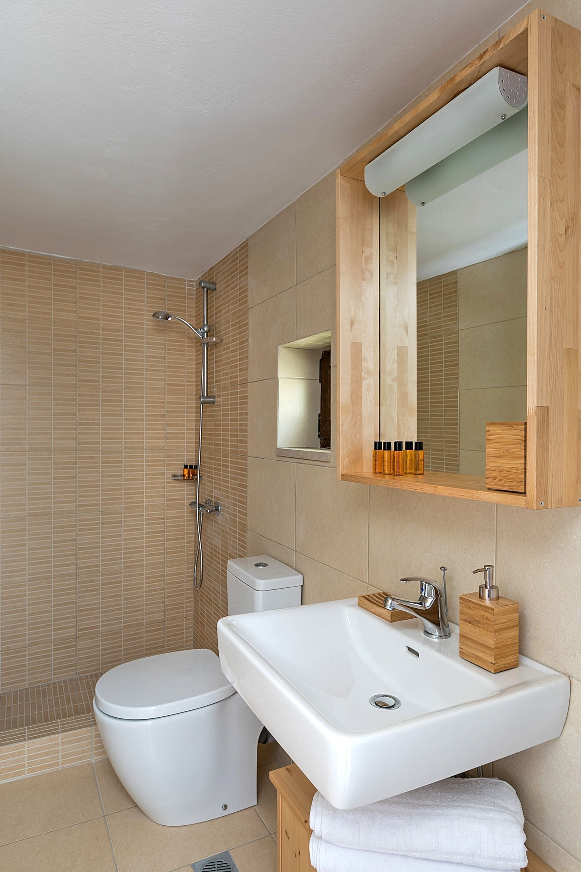 Modern bathroom with shower, beige tiles, a big white washbasin and a big wooden mirror.