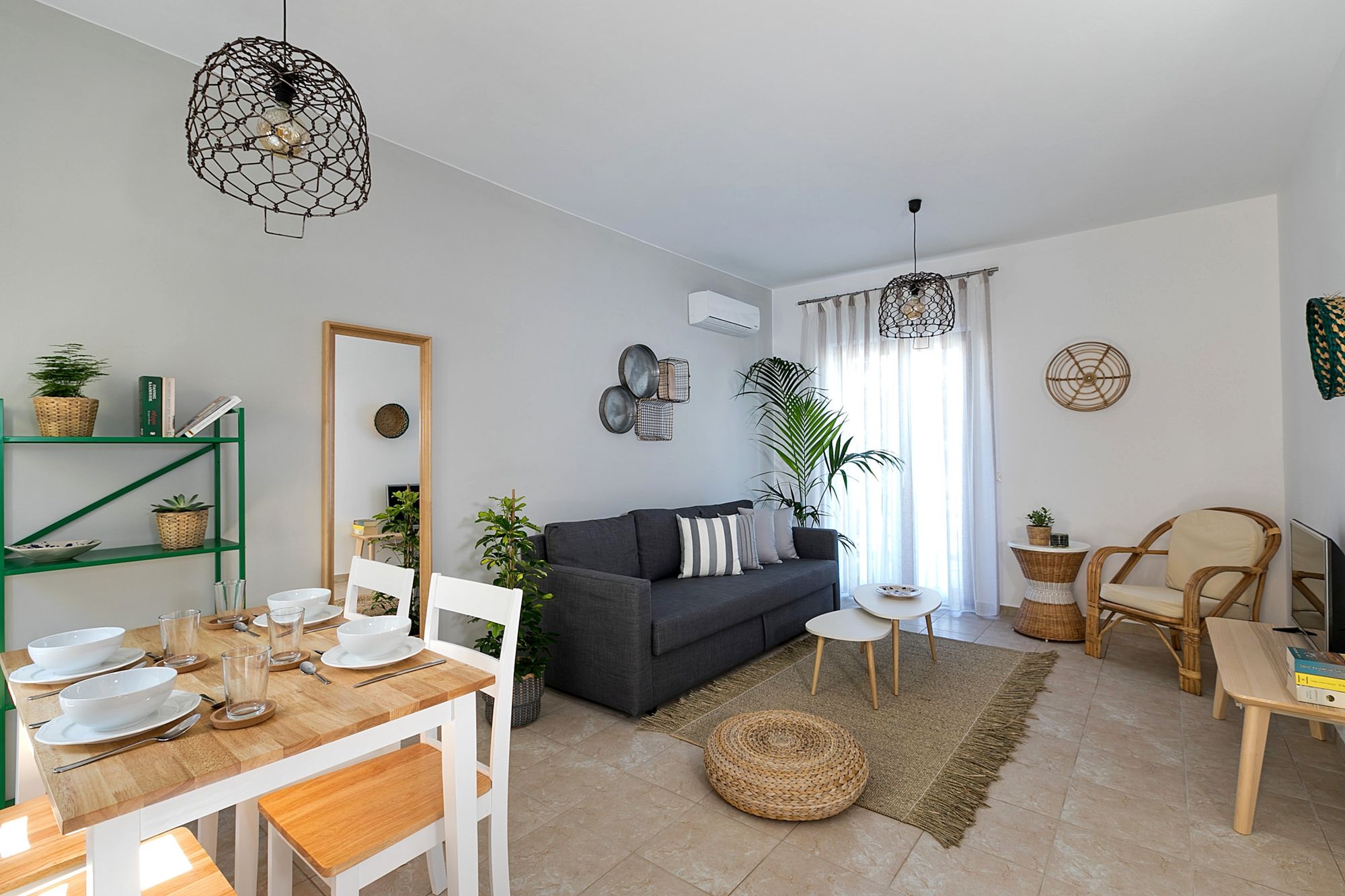 Living room furnished with a gray sofa, an armchair, a metallic green bookcase, a wooden dining table and modern metallic ceiling lights.