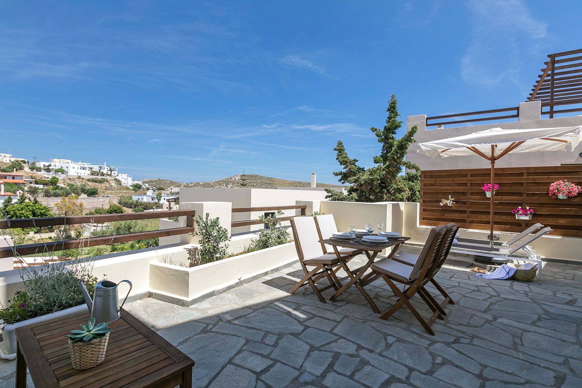 Spacious veranda with a wooden dining table, two sunbeds, a wooden coffee table and flower pots.