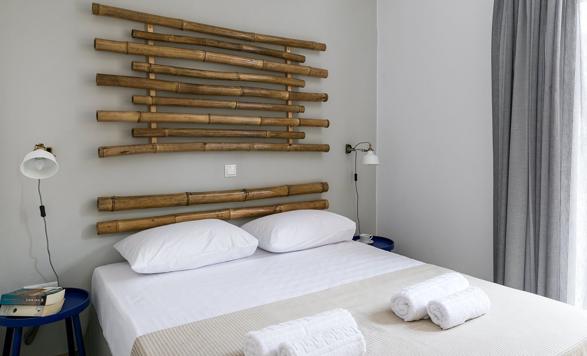 Bedroom with a double bed, two metallic blue bedside tables, modern white-gold wall lights and wooden masts on the wall.