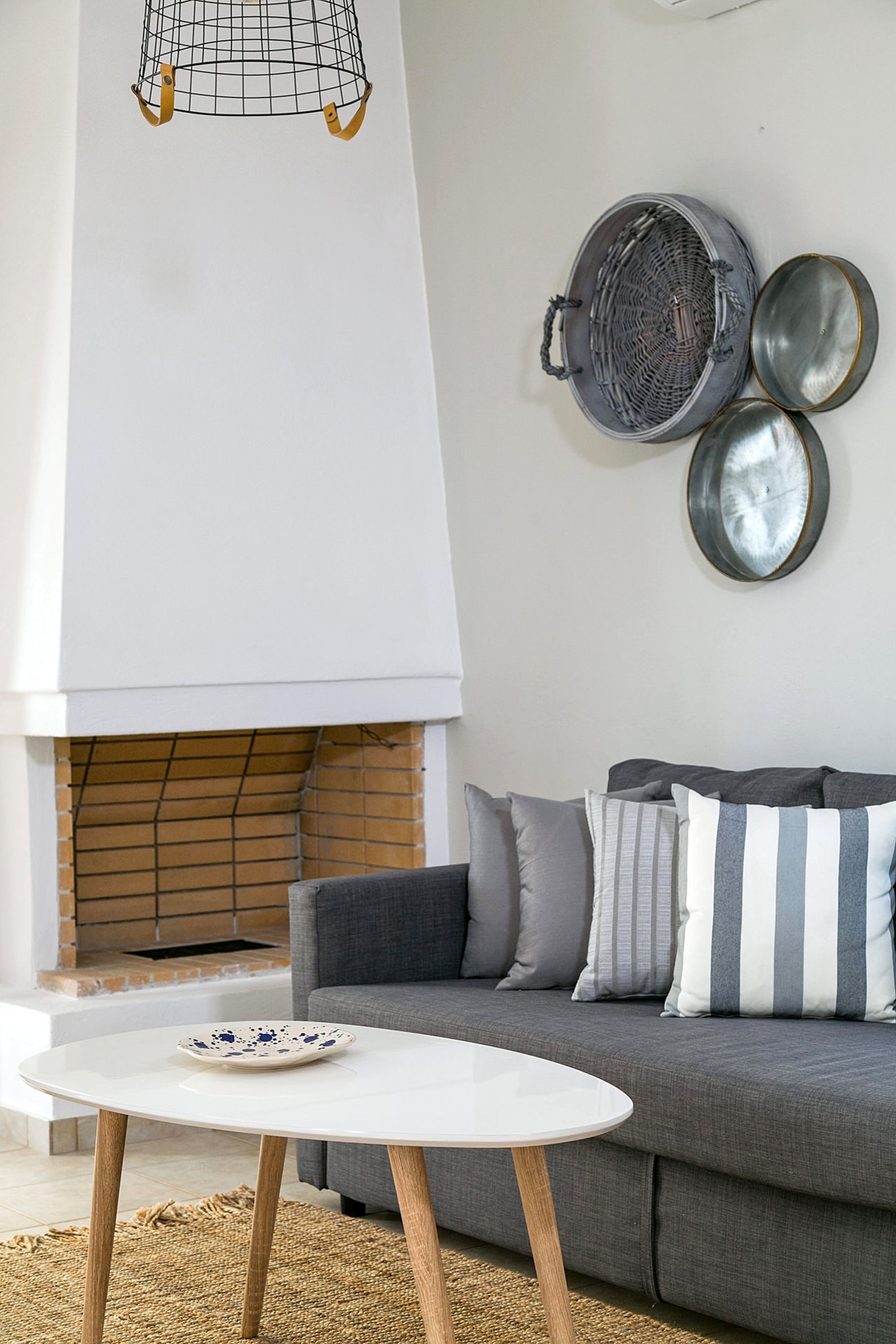 A white fireplace in a modern living room with a gray sofa, a white wooden coffee table and metallic decorative objects on the wall over the sofa.