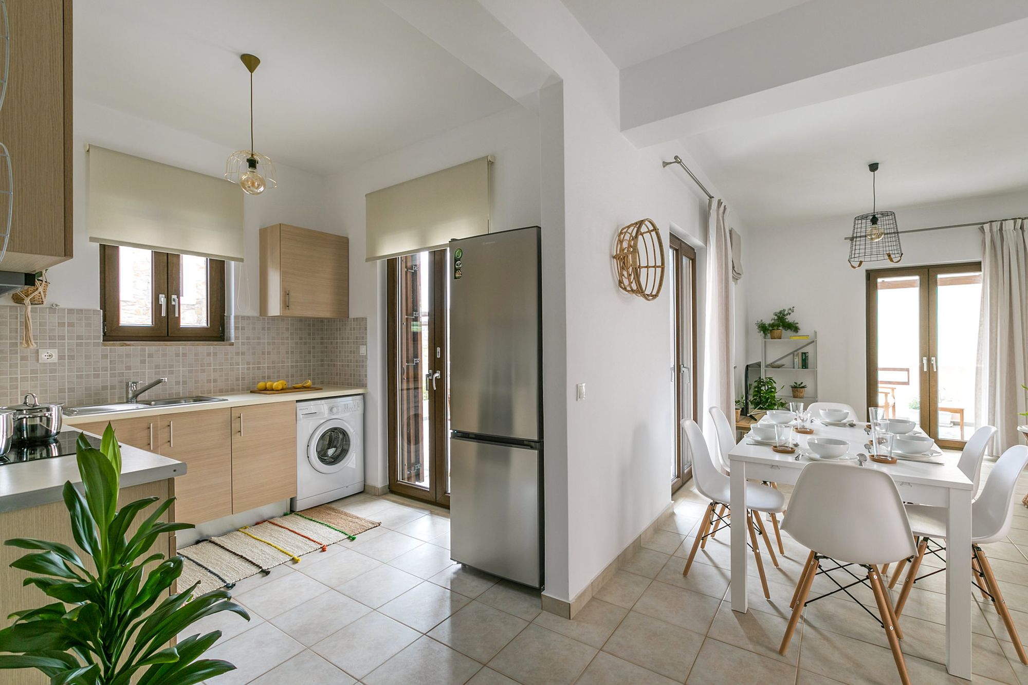 Modern kitchen equipped with a big inox fridge, a washing machine and a white dining table with six chairs.