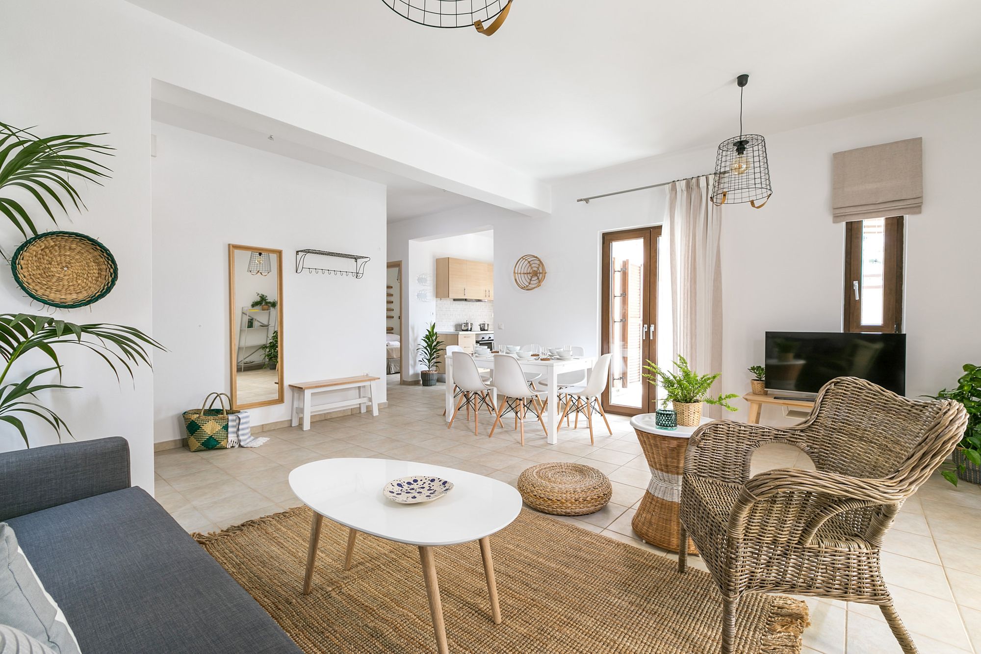 Spacious living room decorated in boho style with a gray sofa, a white wooden coffee table, an armchair and flowerpots.