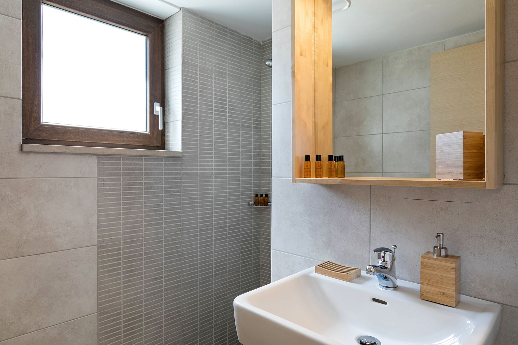 A big white washbasin and a wooden mirror in a gray modern bathroom.