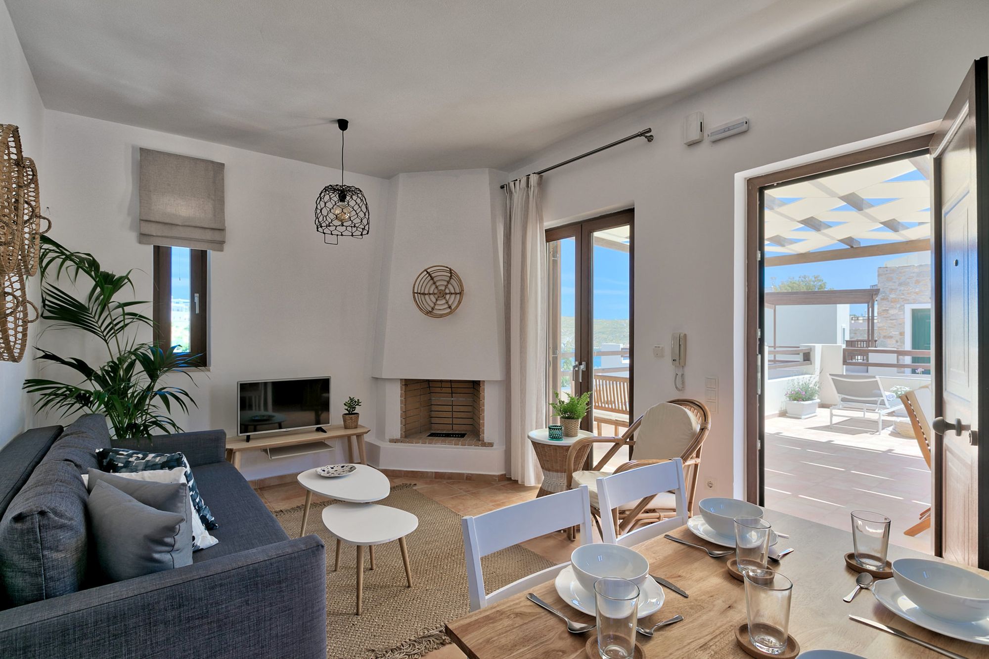 Living room with a white fireplace, a gray sofa, a dining table and wall decoration with wicker objects.