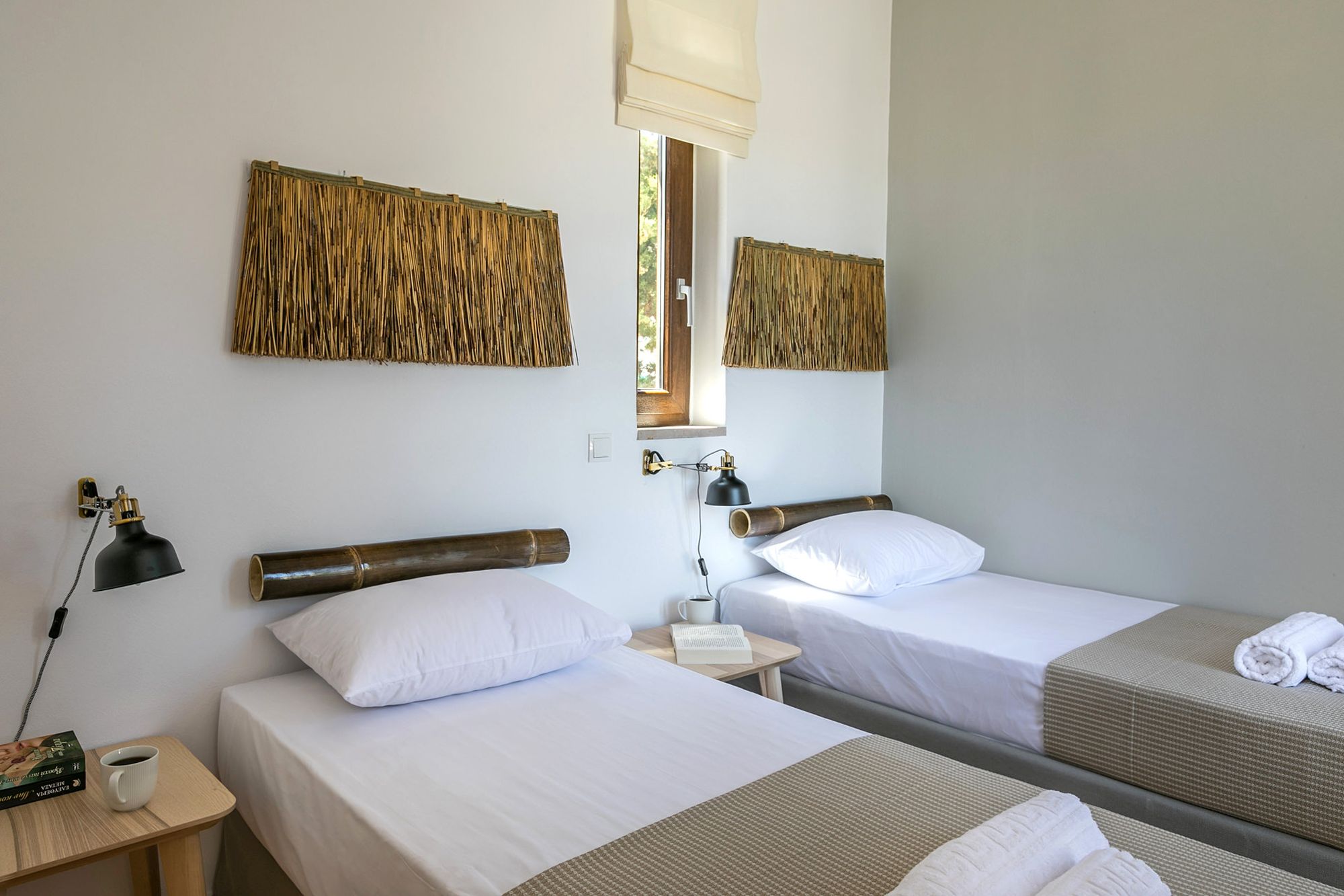 A twin bedroom with modern black wall lights, wooden bedside tables and decoration with bamboo masts and wall wicker objects over the beds.