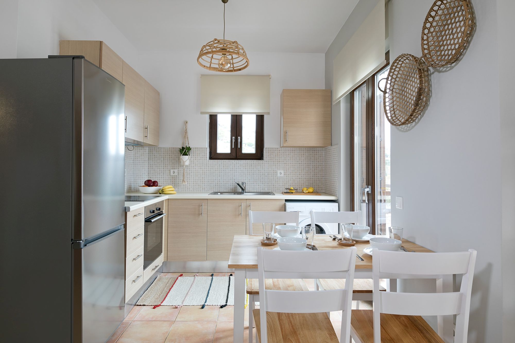 A modern kitchen with beige cabinets, a big inox fridge, an electric cooker oven and a wooden dining table.