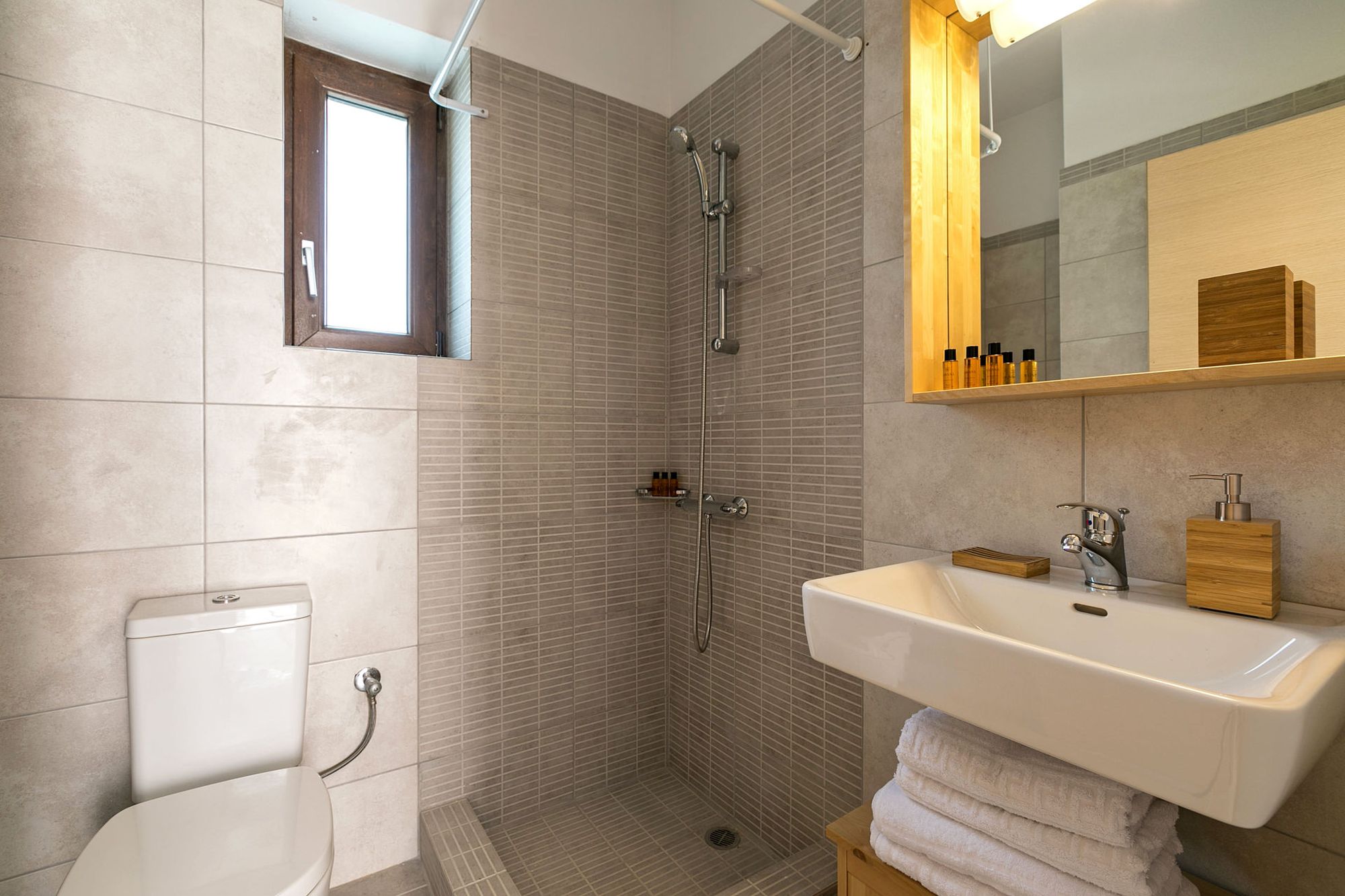 Beige bathroom with shower, a big white washbasin and a big wooden mirror.