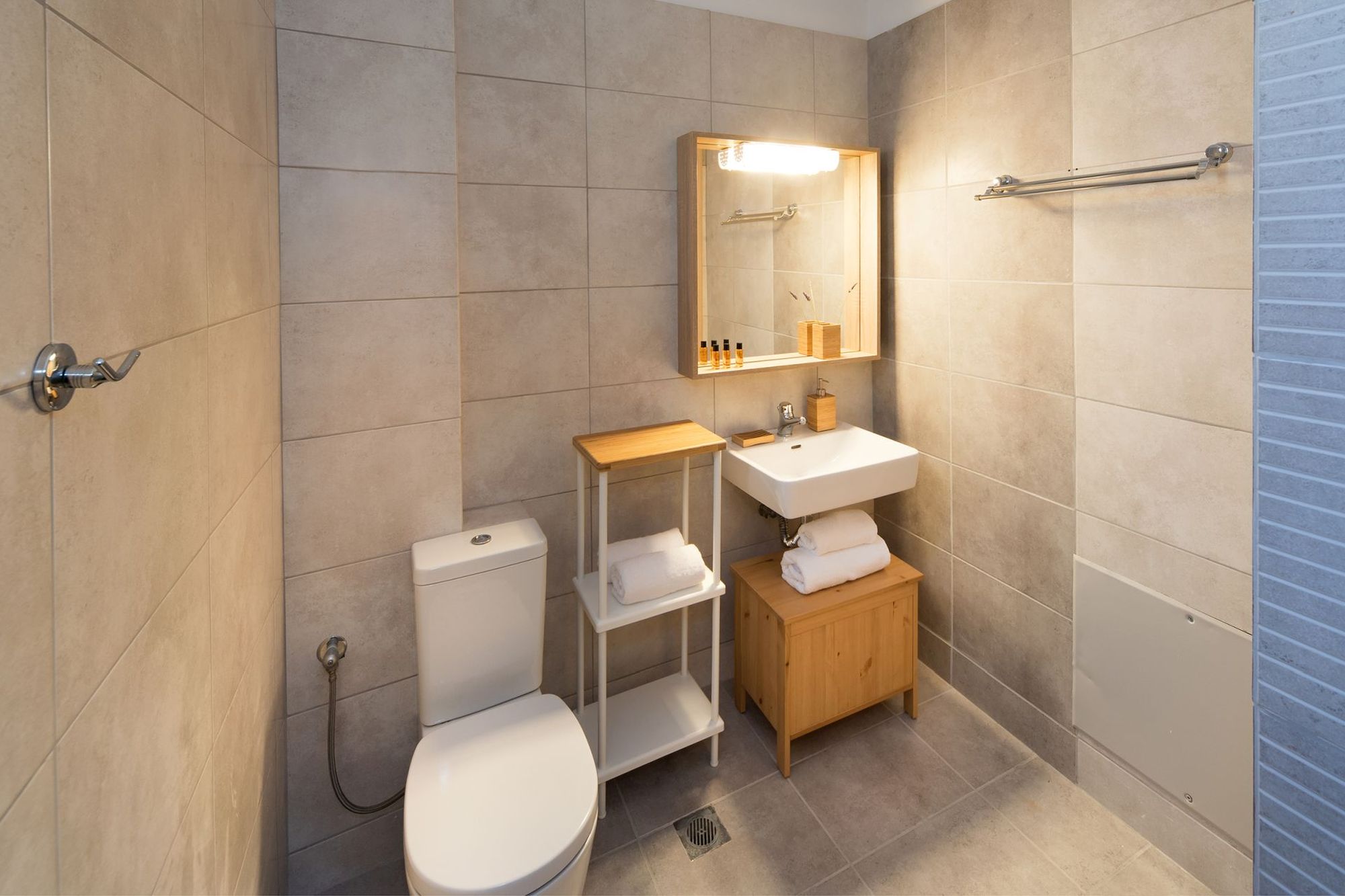 Modern beige bathroom with wooden shelf unit, white washbasin and big wooden mirror.