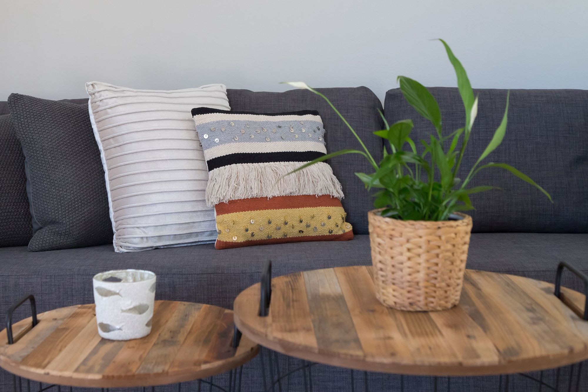 Gray sofa with two colored decorative pillows and two round metallic-wooden coffee tables with a flowerpot.