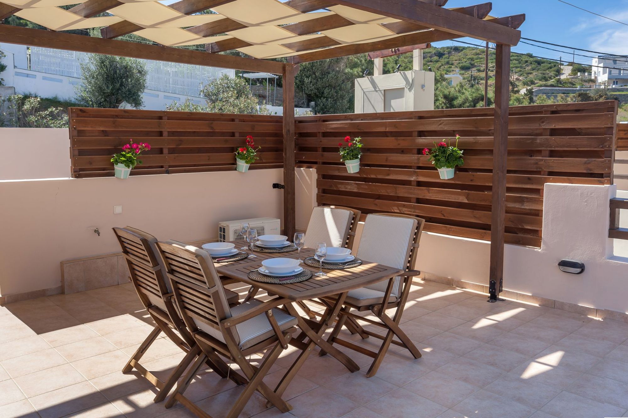 Veranda with pergola and dining table with white tableware set and four chairs.