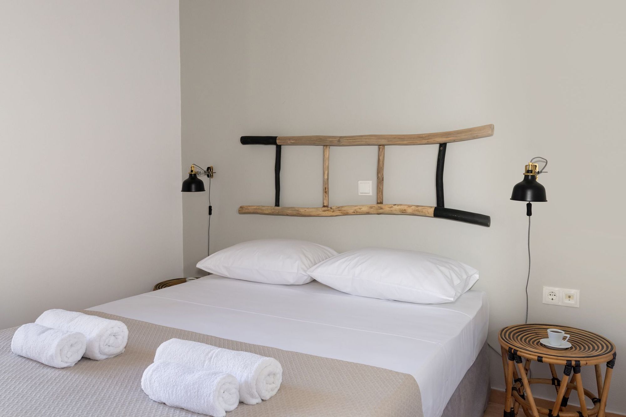 Bedroom with a double bed, wooden bedside tables, black wall lights and a decorative wooden ladder on the wall above the bed.