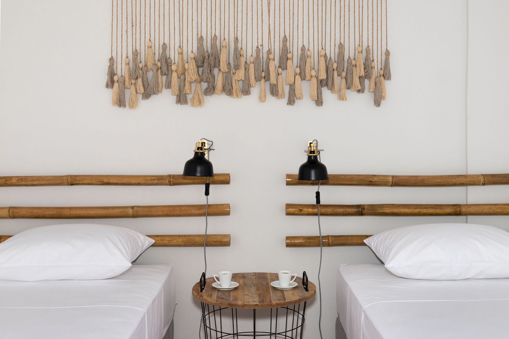 A twin bedroom decorated with a wall macramé, a modern wooden-metallic bedside table and black wall lights.