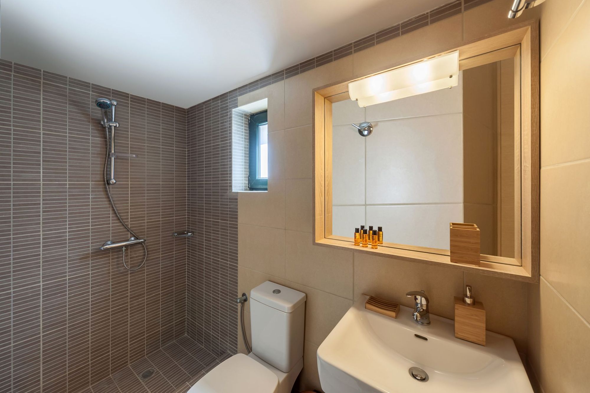 Μοντέρνο μπάνιο με ντουζιέρα σε γκρι και μπεζ αποχρώσεις, ένα μεγάλο λευκό νιπτήρα και ένα μεγάλο ξύλινο καθρέφτη.