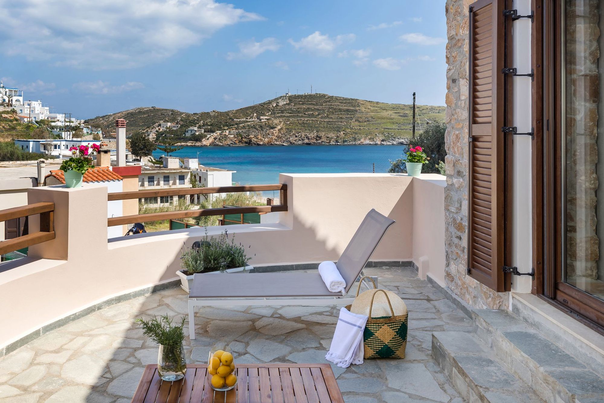 Sea view veranda of a stone-built residence with a sunbed and a wooden coffee table.